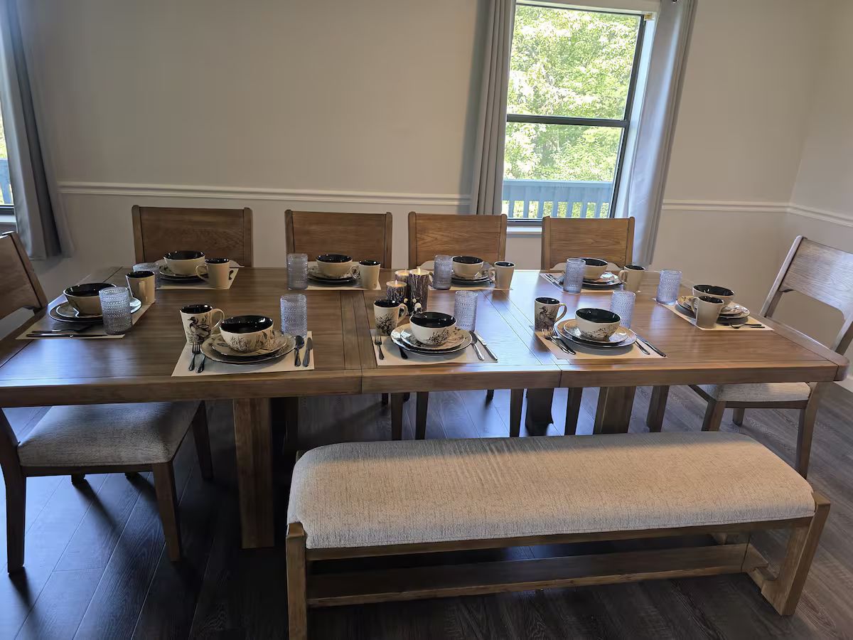A wooden dining table with chairs and a bench beside windows at Family Times Cabin.